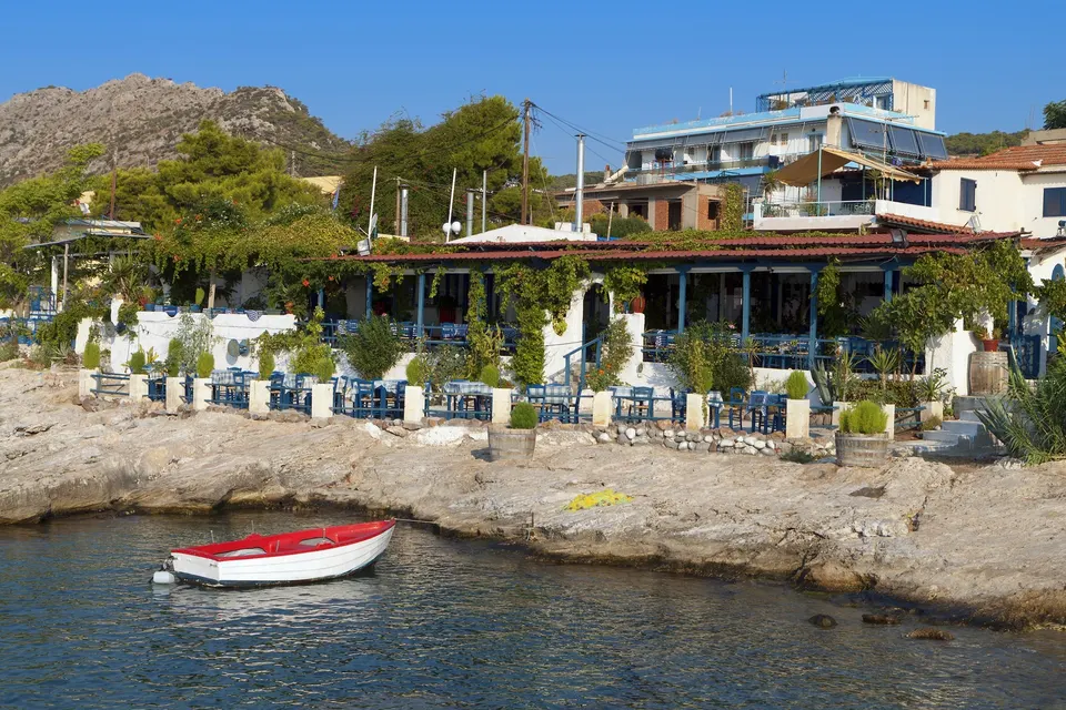 Rød og hvid robåd ved klippekysten foran en taverna i Agia Marina på Aegina
