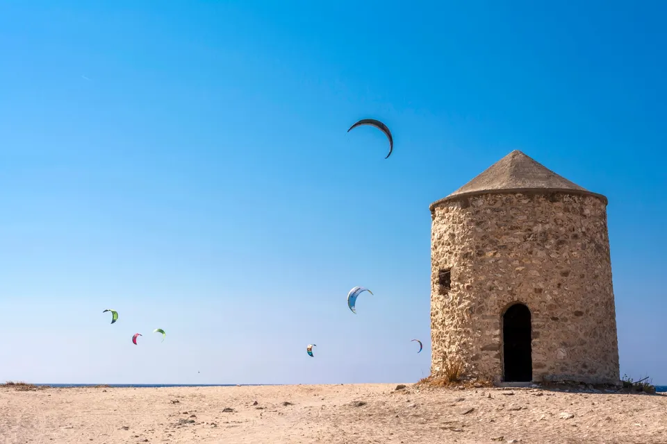 Gammel stenvindmølle på stranden ved Agios Ioannis med farverige kites på himlen