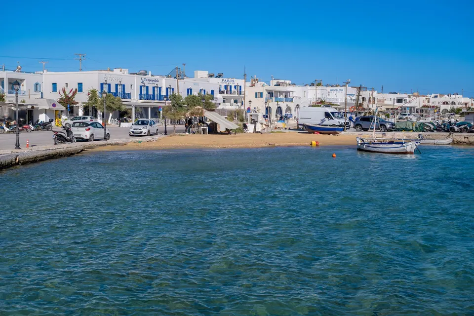 Havnefronten i Antiparos by med hvide huse og en lille strand set fra vandet