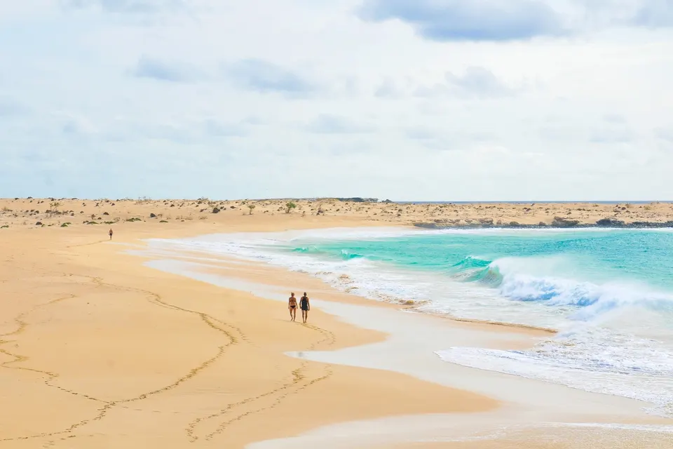 Par går på en lang, øde sandstrand med bølger på Boa Vista