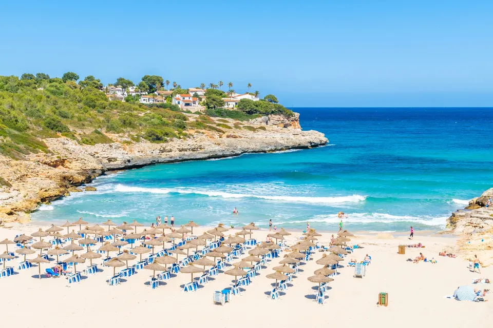 Sandbugten Cala Mandia på Mallorca med parasoller, turkis vand og ferieboliger på klipperne