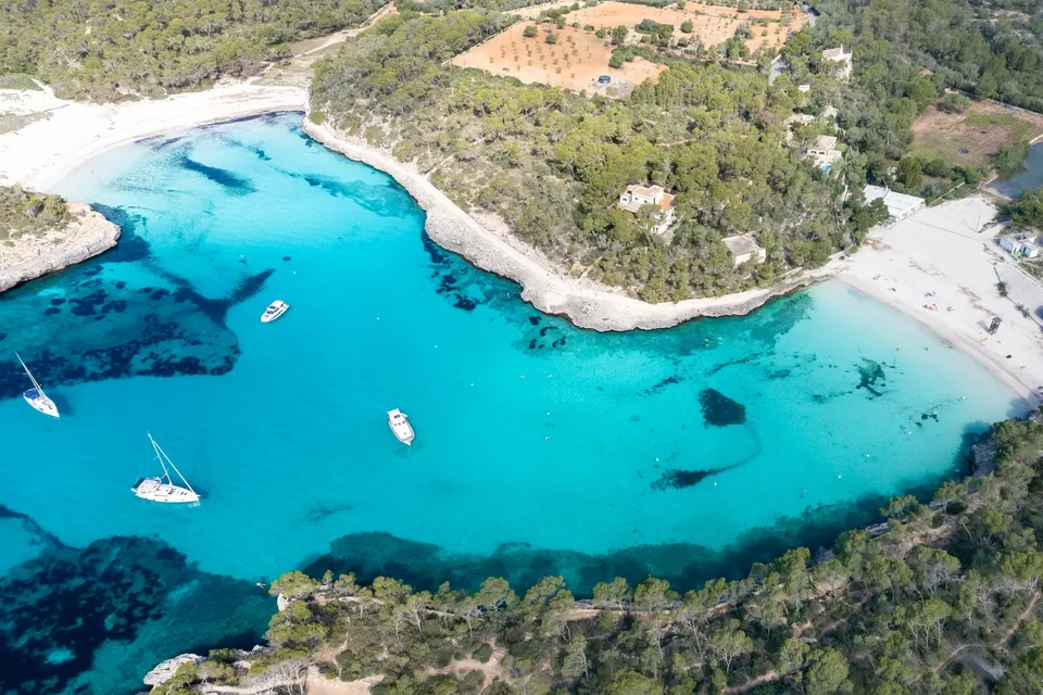 Luftfoto af Cala Mondragós to sandbugter med turkisblåt vand, sejlbåde og fyrreskov
