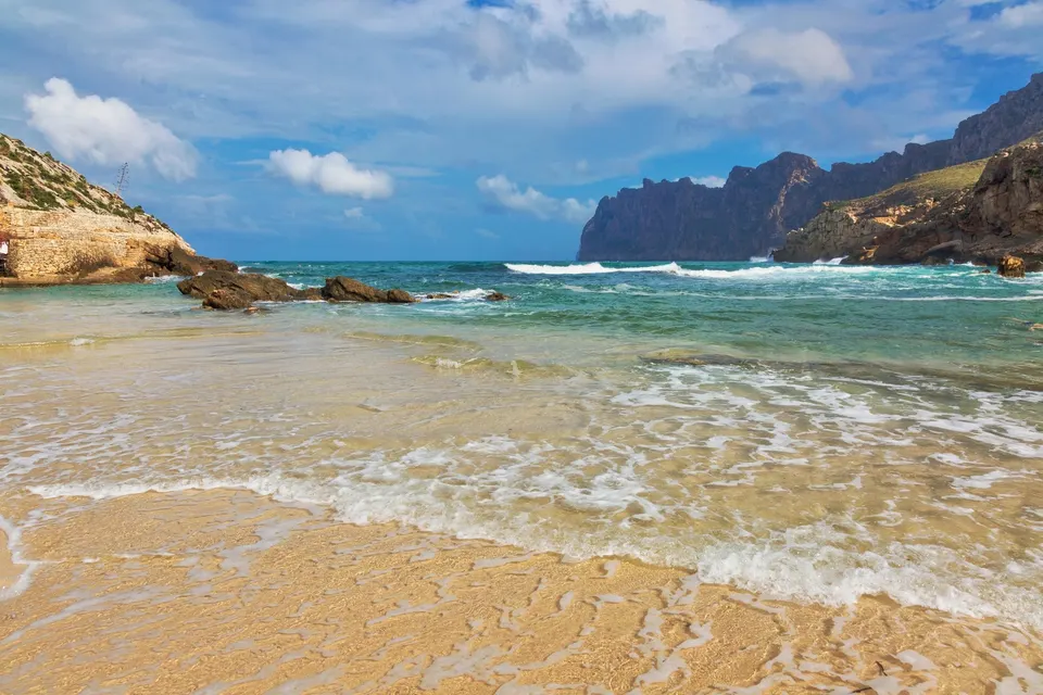 Sandstrand og klart vand i Cala San Vicente med de stejle kalkklipper ved Cavall Bernat i baggrunden