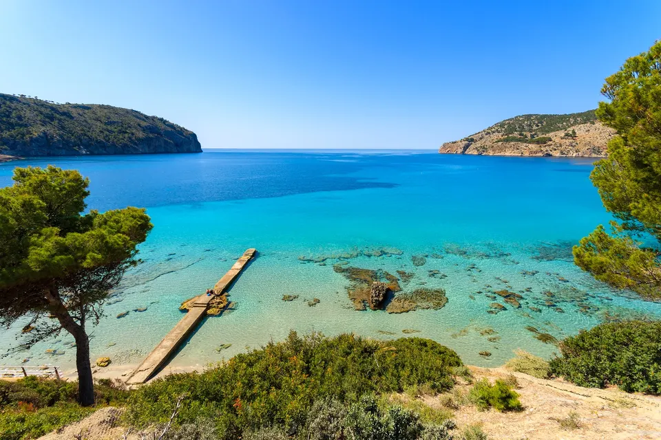 Turkisblå bugt ved Camp de Mar med fyrretræ, gammel mole og klippeforbjerge