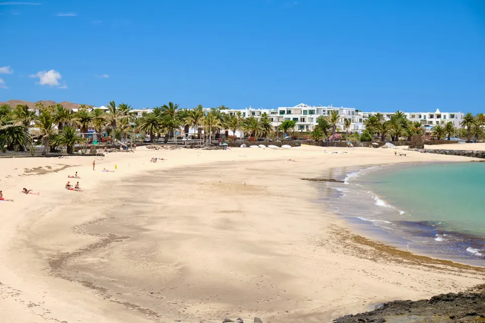 Den lyse sandstrand i Costa Teguise med palmer og hoteller bagved