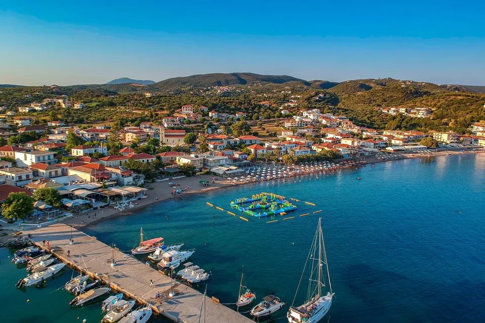 Luftfoto af havnemolen med både, stranden og byen i Finikounda i aftenlys