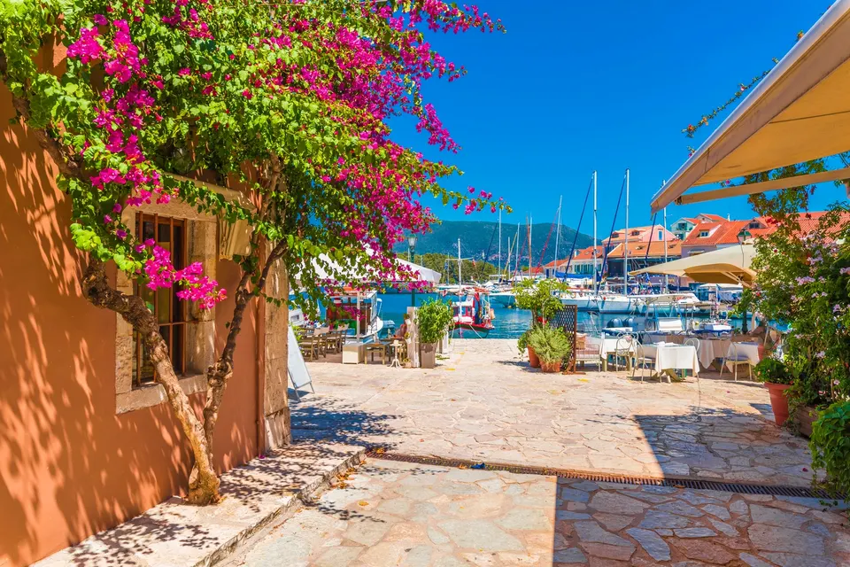 Bougainvillea ved et orange hus med restauranter og sejlbåde i havnen i Fiskardo