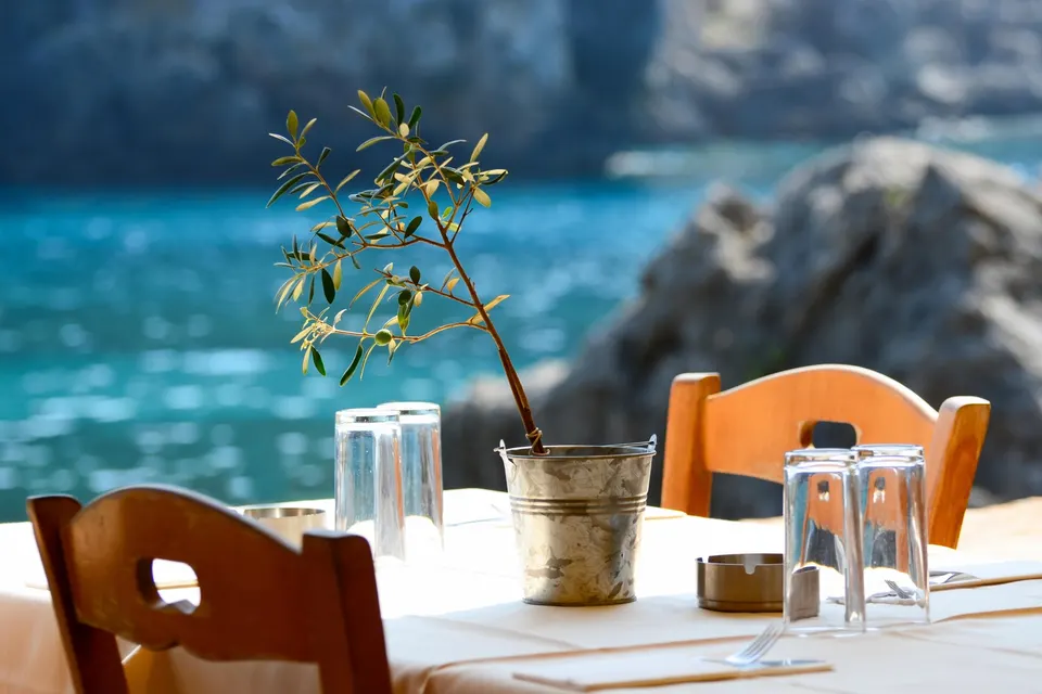 Bord med glas og et lille oliventræ i spand på en taverna ved det turkise hav