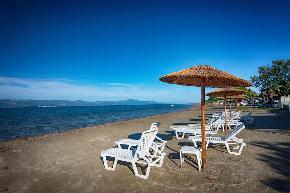 Stranden i Kavos med stråparasoller og hvide liggestole og fastlandet i baggrunden
