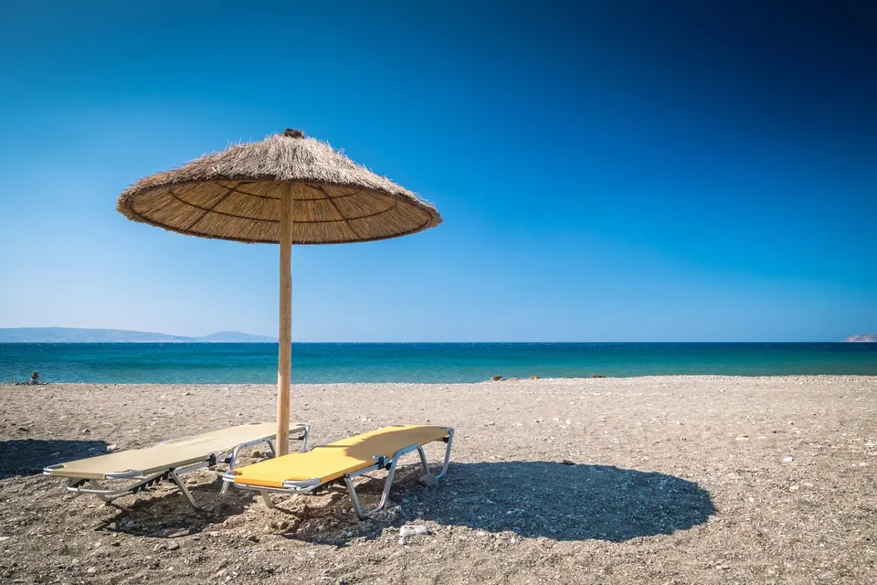 Stråparasol og to liggestole på en gruset sandstrand ved havet