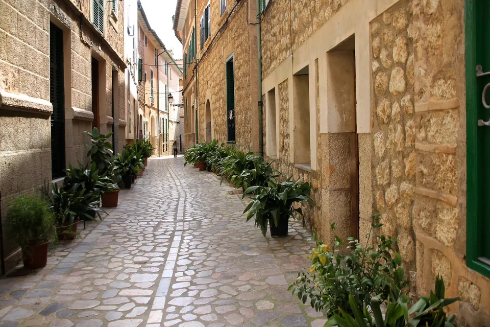 Smal brostensgade med stenhuse og potteplanter i en by på Mallorca