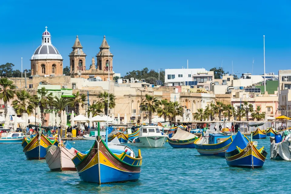 De farvede luzzu-både i havnen i Marsaxlokk med kirken bagved