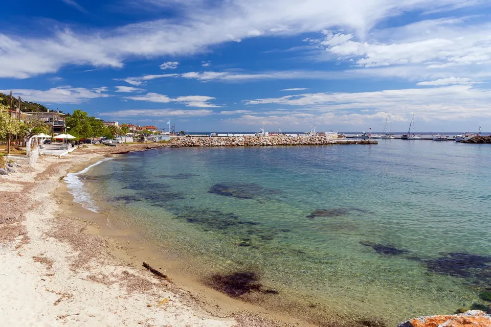 Sandstranden i Nea Skioni med klart vand og havnemolen bagved