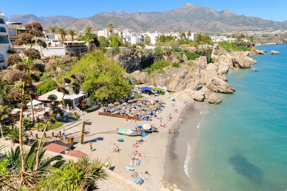 Stranden under Balcón de Europa i Nerja med klipper og palmer