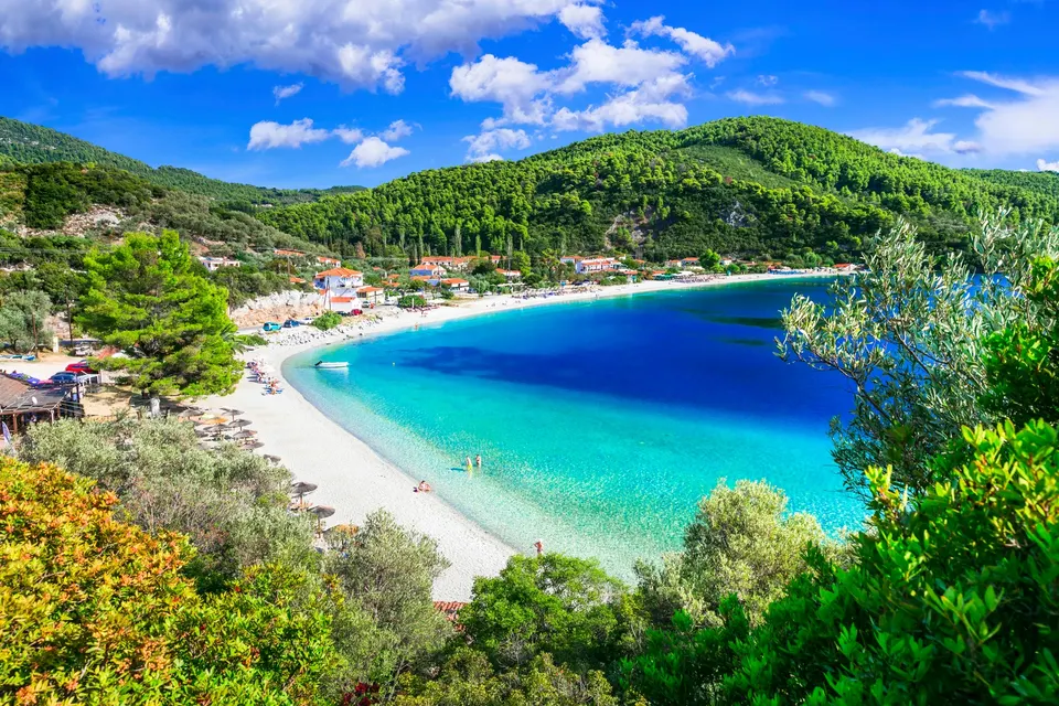 Panormos-stranden set fra skrænten gennem grønt med hvide sten, parasoller og turkis vand