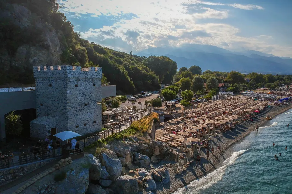 Stranden i Paralia Panteleimonos med det gamle stentårn, parasoller og bjergene i aftenlys