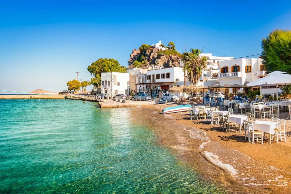 Strand og tavernaborde ved vandkanten i Skala på Patmos med turkis vand