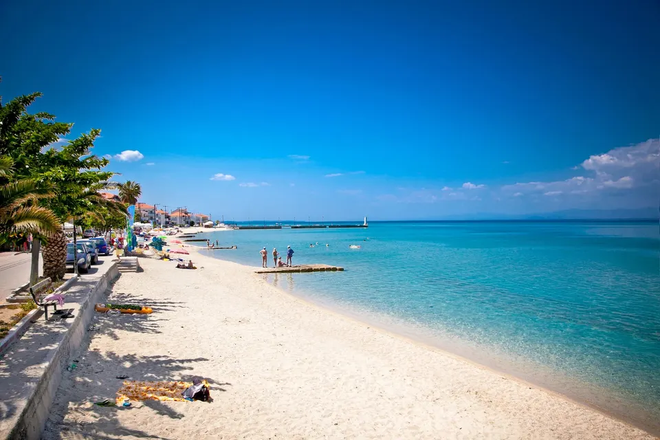Sandstranden langs promenaden i Pefkochori med palmer og klart vand