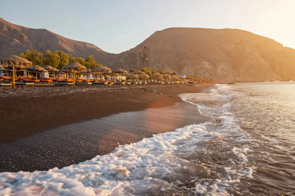 Den sorte strand i Perissa ved solopgang med parasoller og Mesa Vouno bagved