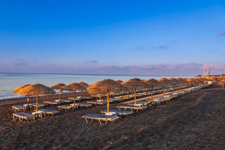 Lange rækker af stråparasoller på stranden i Perivolos i blødt morgenlys
