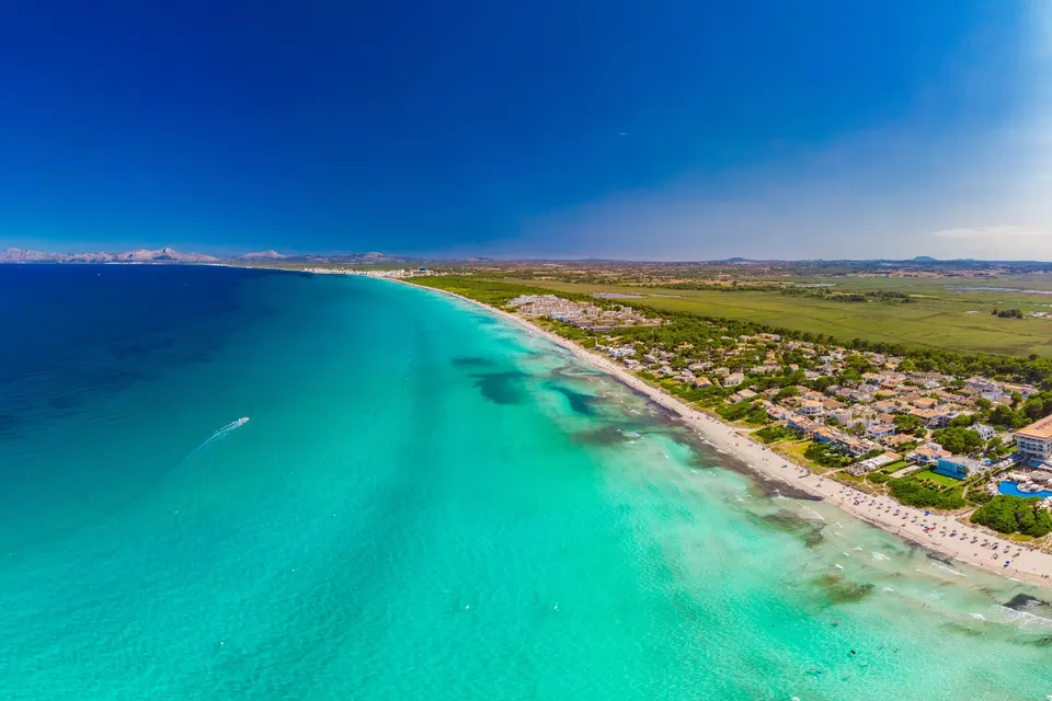 Luftfoto af den lange hvide sandstrand ved Playa de Muro med lavt turkis vand og hoteller bag stranden