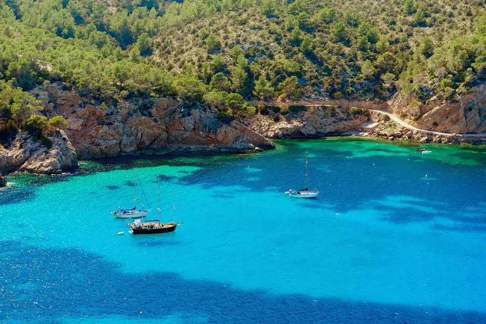 Turkis vand og både under de skovklædte klipper ved Port de Sant Miquel