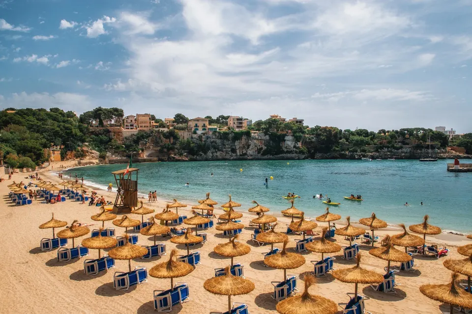 Sandstranden inderst i bugten i Porto Cristo med parasoller, klart vand og byens huse på klipperne