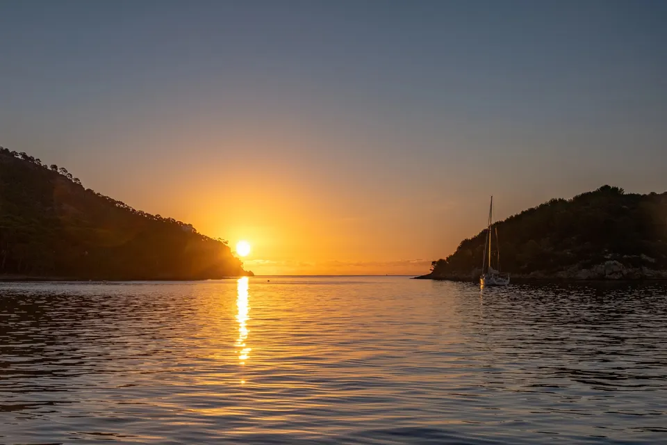 Solopgang over en rolig bugt med en sejlbåd for anker på Mallorca