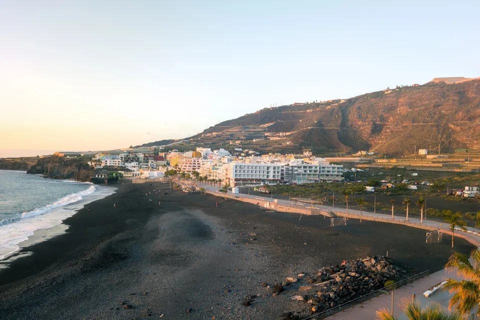 Den sorte strand og promenaden med palmer i Puerto Naos i aftenlys