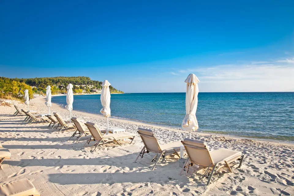 Liggestole og parasoller i det lyse sand på stranden ved Sani